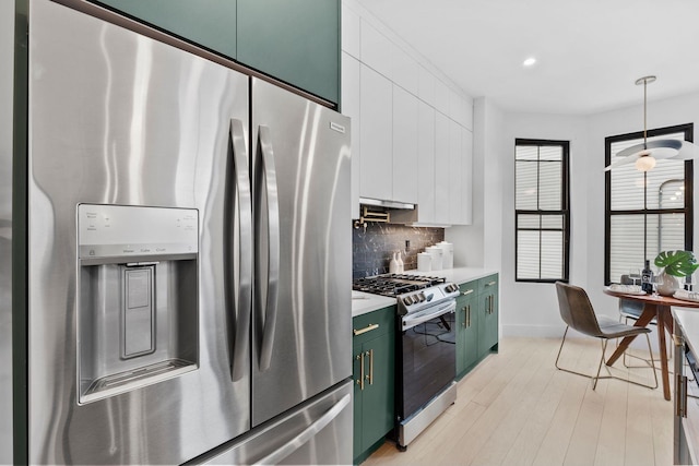 kitchen with green cabinetry, light wood-style flooring, light countertops, appliances with stainless steel finishes, and backsplash