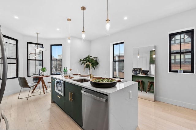 kitchen featuring a sink, stainless steel appliances, an island with sink, and light wood finished floors