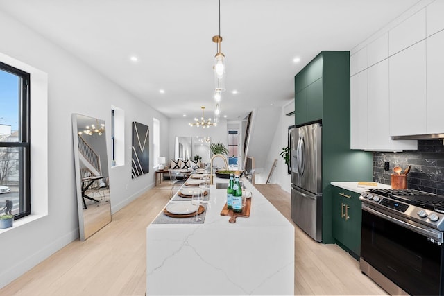 kitchen featuring modern cabinets, a center island with sink, appliances with stainless steel finishes, an inviting chandelier, and decorative backsplash