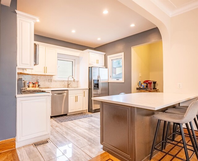 kitchen featuring white cabinetry, appliances with stainless steel finishes, tasteful backsplash, crown molding, and light wood-type flooring