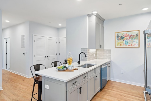 kitchen featuring light wood-type flooring, backsplash, sink, dishwasher, and a breakfast bar area