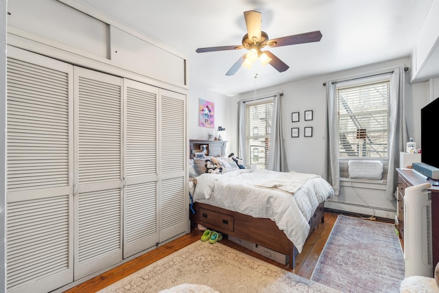 bedroom featuring a ceiling fan, baseboard heating, a closet, and hardwood / wood-style floors