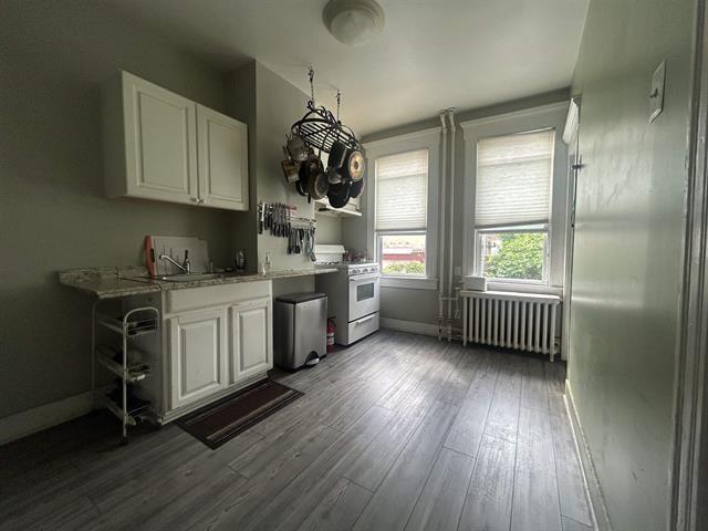 kitchen featuring hardwood / wood-style floors, gas range gas stove, radiator heating unit, and white cabinetry