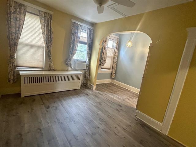 empty room with wood-type flooring, radiator heating unit, and ceiling fan