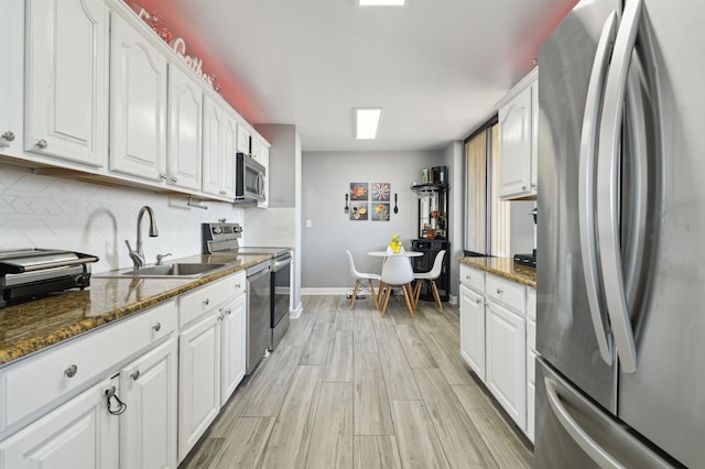 kitchen with appliances with stainless steel finishes, a sink, white cabinetry, and tasteful backsplash