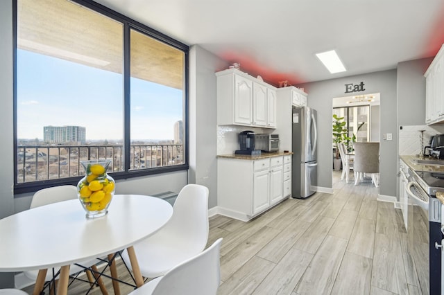 kitchen with light wood-style flooring, stainless steel appliances, white cabinets, a view of city, and tasteful backsplash