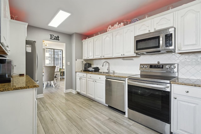 kitchen with stainless steel appliances, a sink, white cabinetry, and decorative backsplash