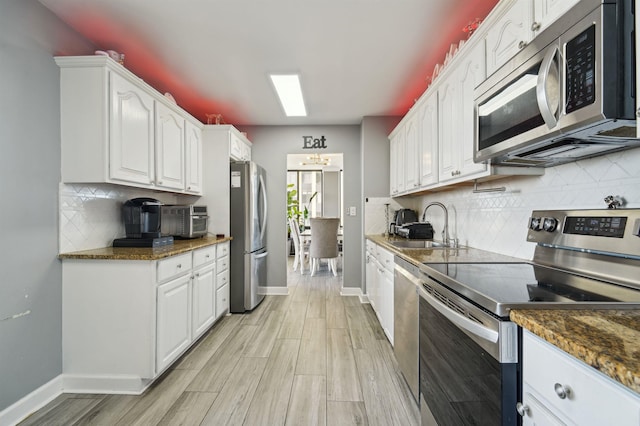 kitchen featuring appliances with stainless steel finishes, white cabinets, a sink, and baseboards