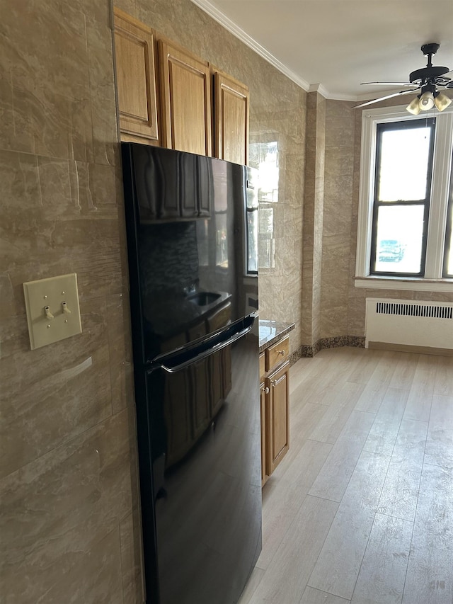 kitchen featuring brown cabinetry, radiator, freestanding refrigerator, and crown molding