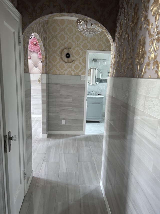 hall featuring a wainscoted wall, wallpapered walls, arched walkways, a sink, and tile walls