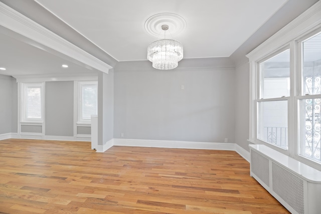 spare room with crown molding, an inviting chandelier, light wood-type flooring, and radiator