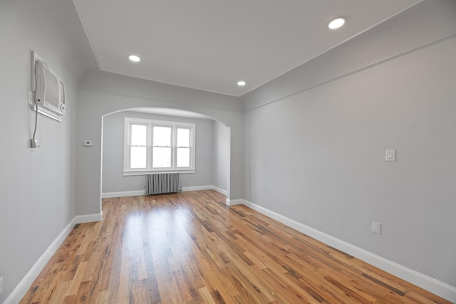 unfurnished room with a wall mounted AC, radiator heating unit, and light hardwood / wood-style flooring