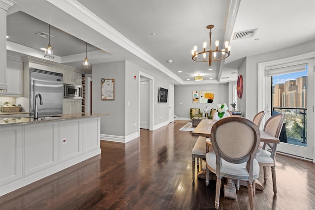 dining space with sink, crown molding, dark wood-type flooring, an inviting chandelier, and a tray ceiling