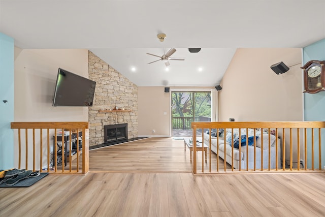 living area with ceiling fan, wood finished floors, a stone fireplace, vaulted ceiling, and baseboards