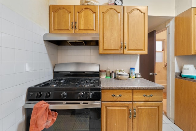 kitchen featuring backsplash, light tile patterned floors, under cabinet range hood, and gas range