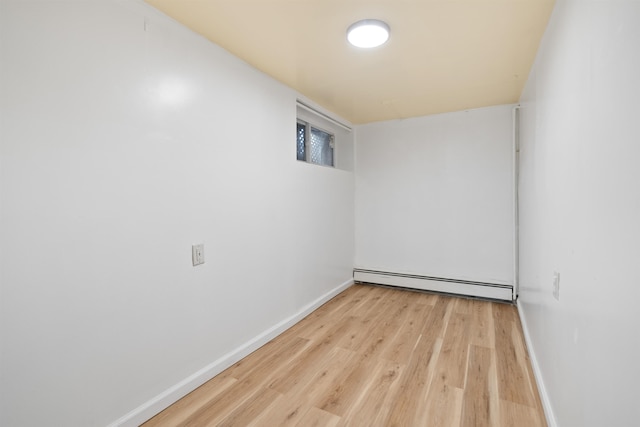 spare room featuring a baseboard heating unit, baseboards, and light wood finished floors