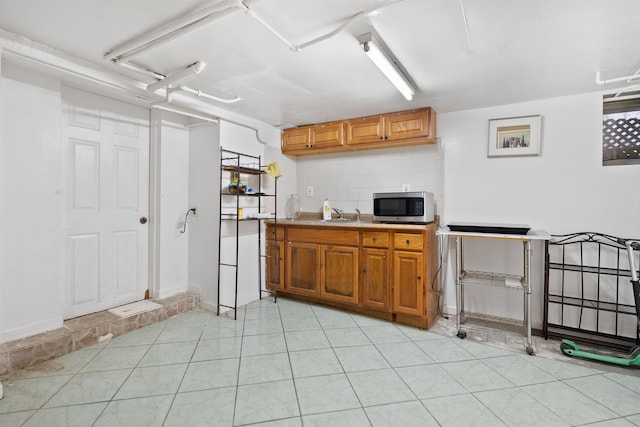 kitchen with light tile patterned floors, stainless steel microwave, brown cabinets, light countertops, and backsplash