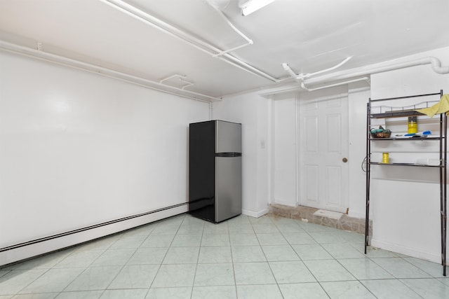 basement with a garage, freestanding refrigerator, light tile patterned flooring, and a baseboard radiator