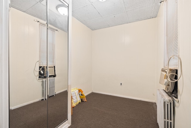 interior space featuring a paneled ceiling, radiator heating unit, dark carpet, and baseboards