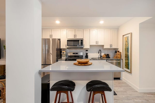 kitchen featuring appliances with stainless steel finishes, backsplash, light hardwood / wood-style floors, white cabinets, and a kitchen bar