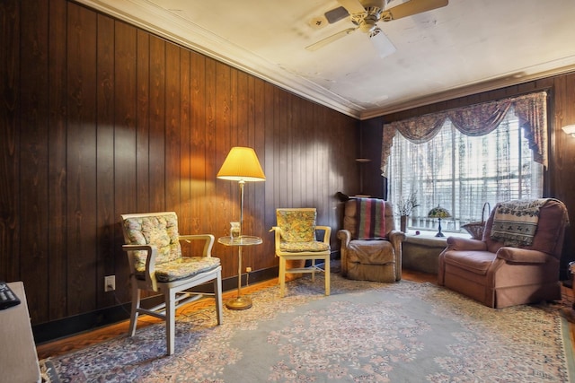 living area with wooden walls, baseboards, ceiling fan, wood finished floors, and crown molding