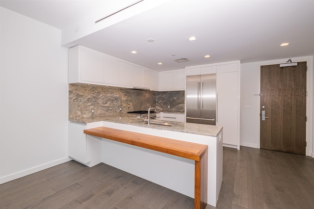 kitchen with white cabinets, kitchen peninsula, light stone countertops, and sink