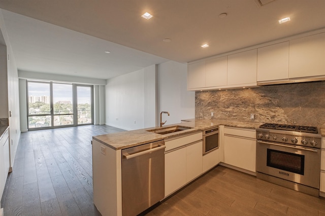 kitchen featuring backsplash, kitchen peninsula, sink, hardwood / wood-style flooring, and appliances with stainless steel finishes