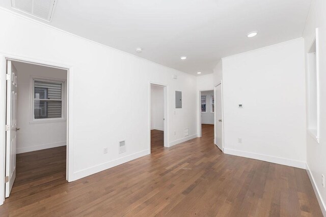 empty room with ornamental molding, electric panel, dark wood-style flooring, baseboards, and recessed lighting