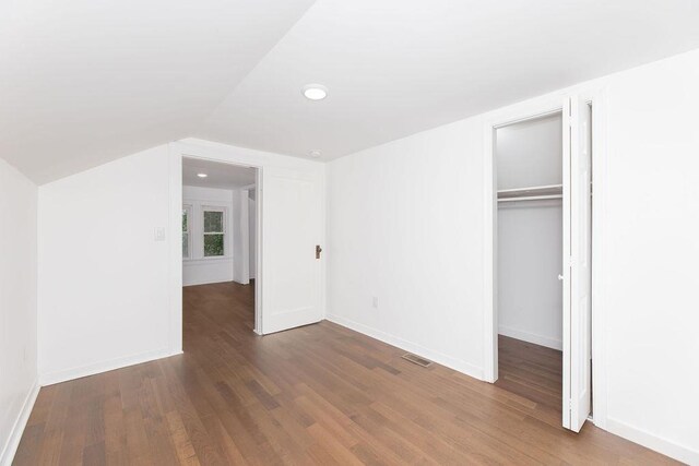 unfurnished bedroom featuring wood finished floors, lofted ceiling, a closet, and baseboards