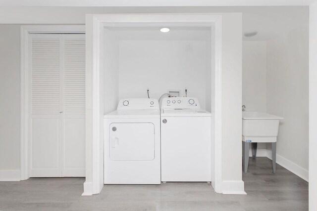 clothes washing area with washer and dryer, baseboards, and light wood finished floors
