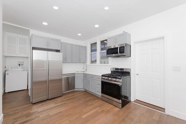 kitchen featuring stainless steel appliances, washer / clothes dryer, gray cabinets, a sink, and backsplash