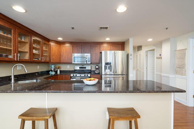 kitchen with visible vents, glass insert cabinets, dark stone counters, appliances with stainless steel finishes, and a sink