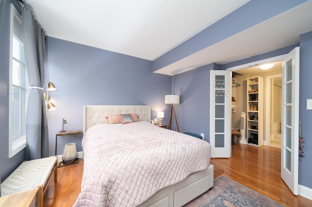 bedroom with wood finished floors, a spacious closet, french doors, and baseboards