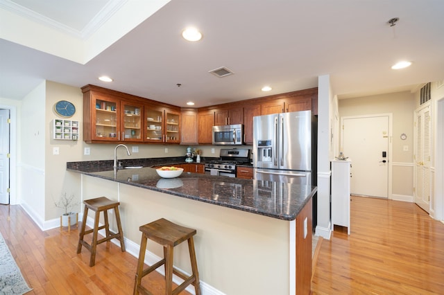 kitchen with visible vents, brown cabinets, dark stone counters, stainless steel appliances, and light wood-type flooring