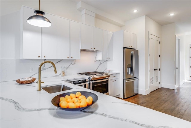 kitchen with light stone countertops, white cabinets, decorative light fixtures, stainless steel appliances, and sink