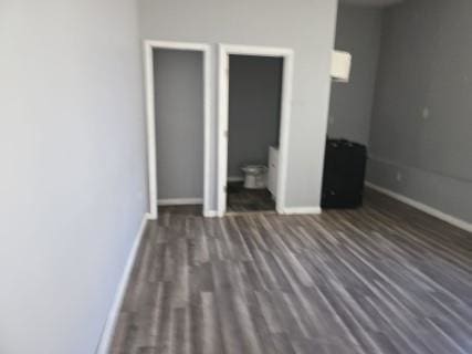 unfurnished bedroom with ensuite bathroom and dark wood-type flooring