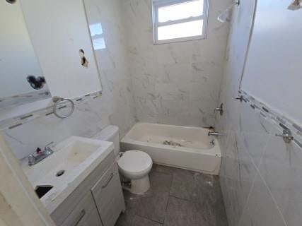 full bathroom with shower / bathing tub combination, vanity, toilet, and tile walls