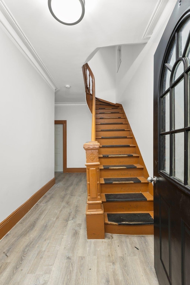 stairway with wood finished floors, baseboards, and ornamental molding