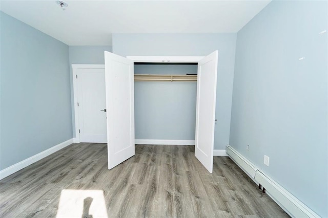 unfurnished bedroom featuring a closet, wood finished floors, baseboards, and a baseboard radiator