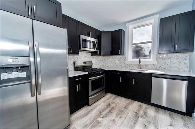 kitchen with light countertops, decorative backsplash, appliances with stainless steel finishes, dark cabinetry, and a sink