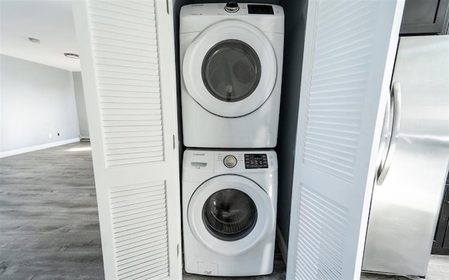 clothes washing area with laundry area, wood finished floors, baseboards, and stacked washing maching and dryer