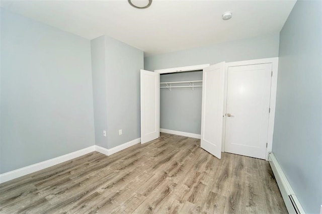 unfurnished bedroom featuring a baseboard heating unit, baseboards, a closet, and wood finished floors