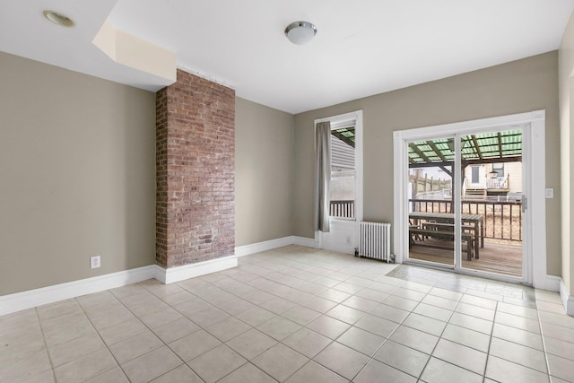 spare room featuring tile patterned flooring, radiator, baseboards, and brick wall