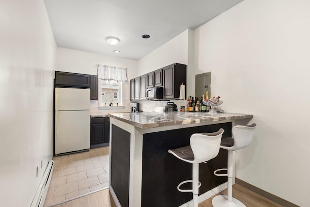 kitchen with a baseboard heating unit, a breakfast bar, light countertops, a peninsula, and freestanding refrigerator