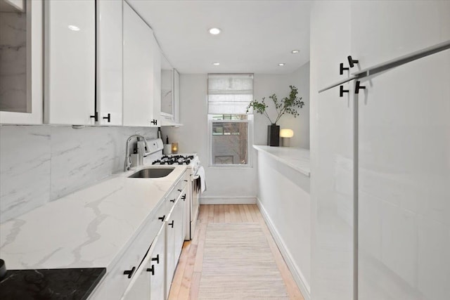 kitchen featuring sink, gas range gas stove, light stone counters, light hardwood / wood-style floors, and white cabinets