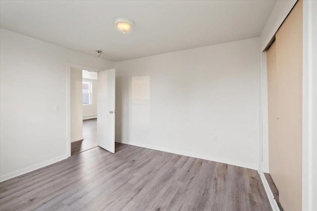 unfurnished bedroom featuring baseboard heating, light wood-type flooring, and a closet