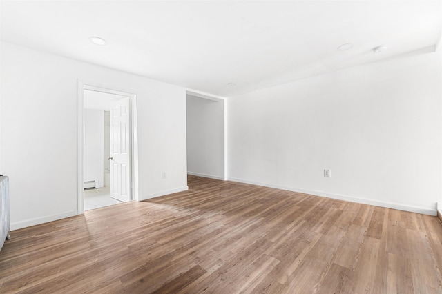 empty room featuring a baseboard radiator, baseboards, and light wood finished floors