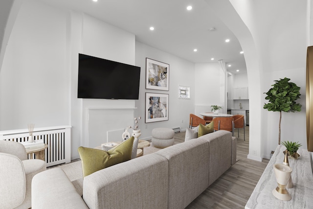 living area featuring wood finished floors, a baseboard radiator, radiator heating unit, recessed lighting, and arched walkways