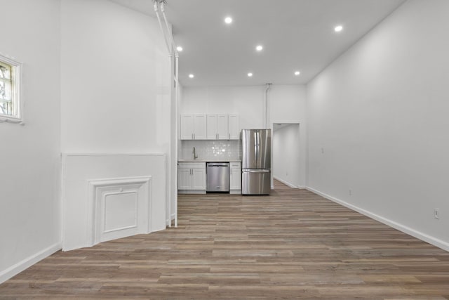 interior space featuring light wood finished floors, a sink, white cabinets, appliances with stainless steel finishes, and backsplash