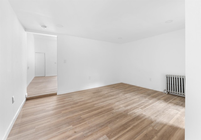 unfurnished room with radiator, baseboards, and light wood-style floors